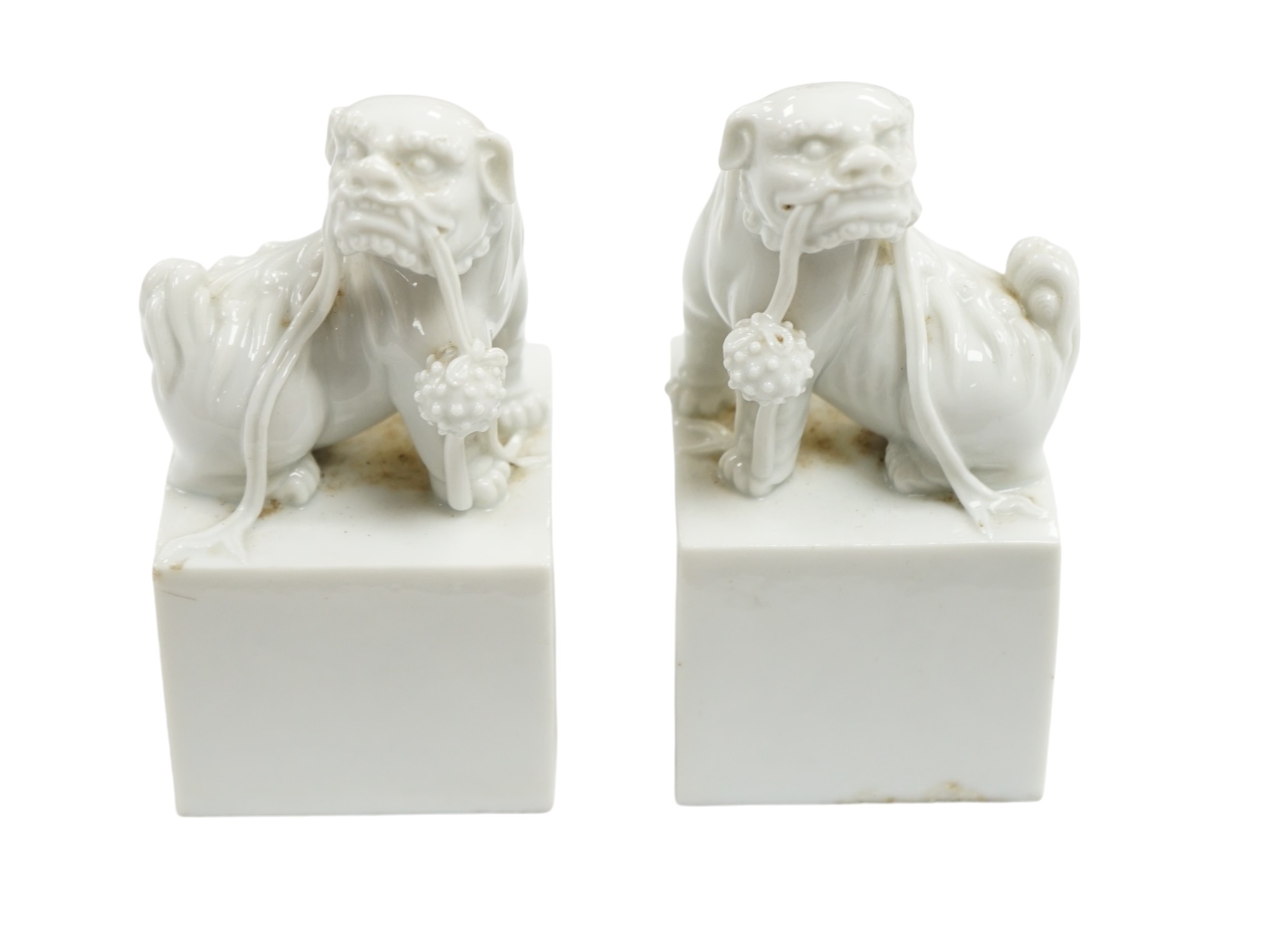 A pair of Japanese Hirado style white glazed porcelain Shishi lion-dog seals and a wooden stand, 10.5cm high. Condition - slight manufacturing glazing losses to base edges